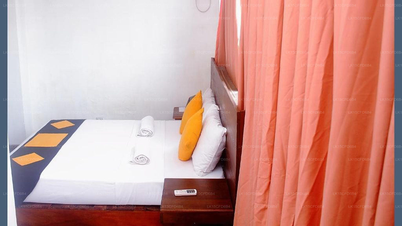 Small bedroom with a bed, pillows, and a nightstand next to an open door with orange curtains.