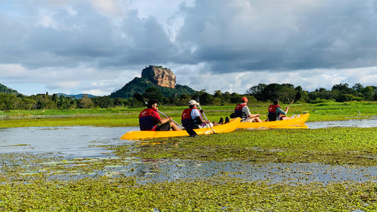 Four people in yellow kayaks paddling on a river with a large rock formation in the background.