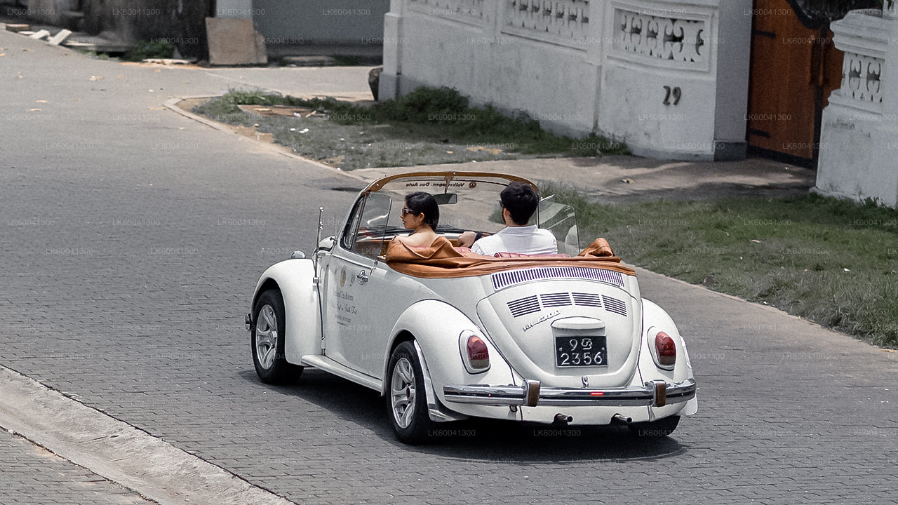 Vintage white convertible car with two people inside on a street.