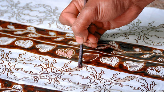 Hand using a tool to create intricate designs on a ceramic plate.