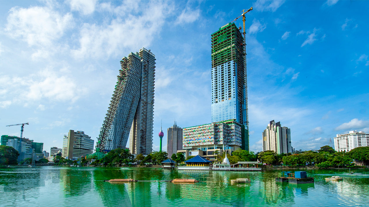 Cityscape with modern buildings and a lake under a blue sky.
