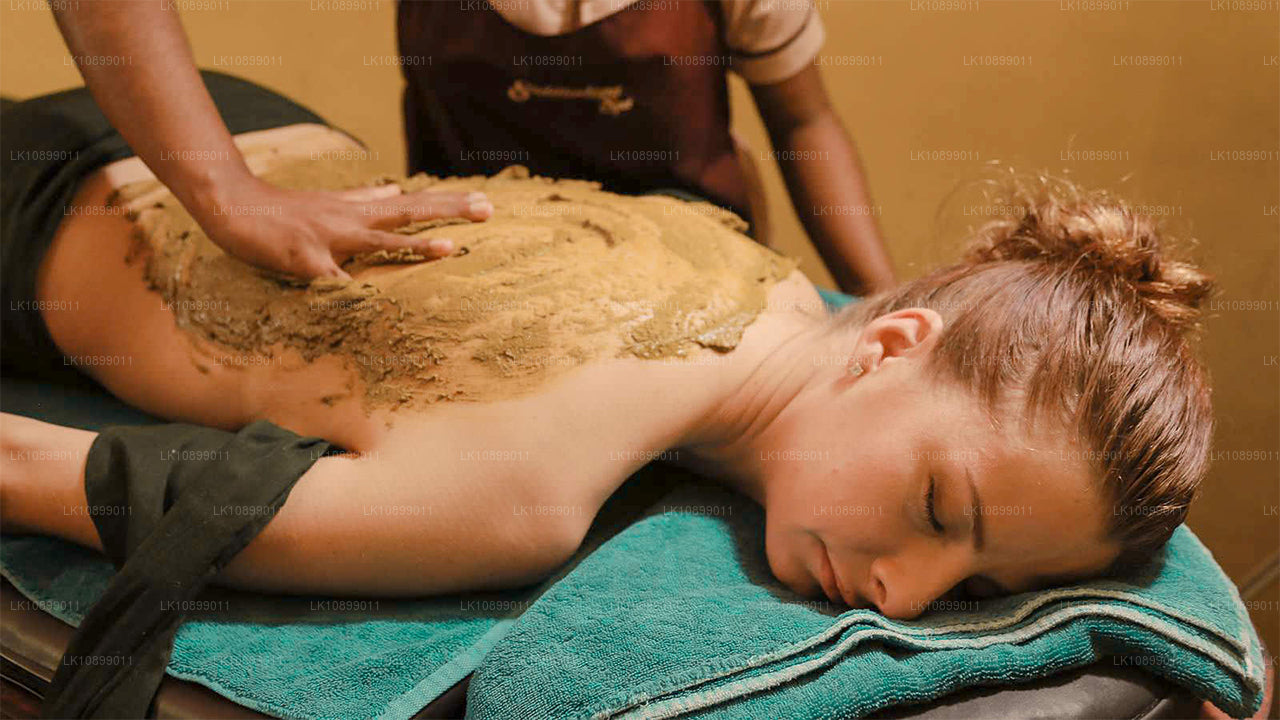 Woman receiving an Ayurvedic herbal body treatment with a paste applied to her back in a spa setting.