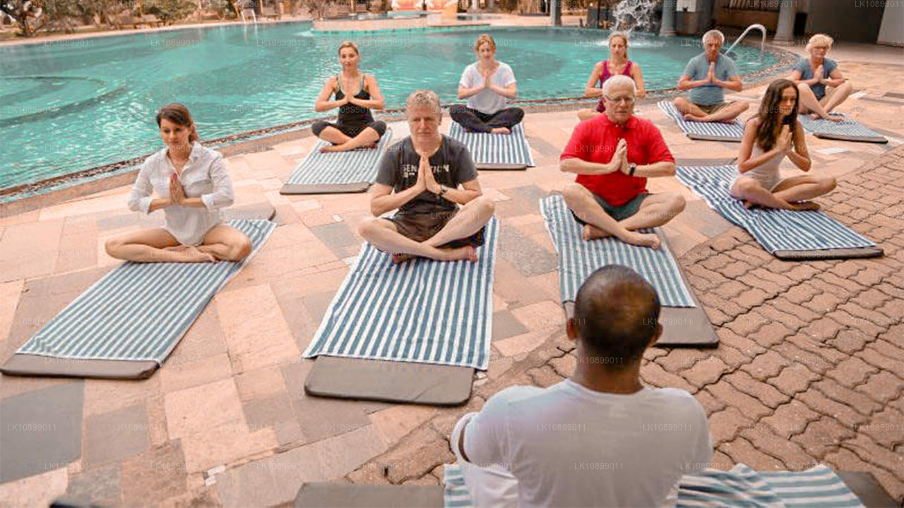 Group of people practicing yoga in a seated prayer pose on mats beside a swimming pool, led by an instructor.
